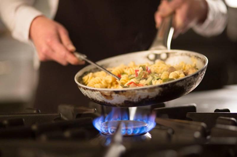 Female cook preparing pasta dish with vegetables on stove